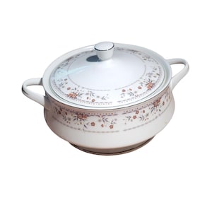 May include: White ceramic casserole dish with a lid, decorated with a floral pattern in peach, brown, and green. It has two handles and a knob on the lid. The design is symmetrical and classic.