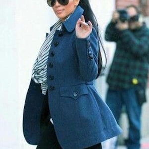 May include: A woman wearing a dark blue coat with a flared bottom, black buttons, and a notched collar. She is also wearing large sunglasses and a black and white striped scarf. The coat has a tailored fit.