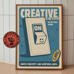 Puede incluir: Un póster enmarcado con un diseño retro. El póster presenta un gran interruptor de luz blanquecino con la palabra "ON" y una cara guiñando un ojo. El texto superior dice "CREATIVE Switch *NO BATTERIES NEEDED". El texto inferior dice "IGNITES CREATIVITY. AND SOMETIMES LAMPS."