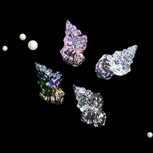May include: An assortment of iridescent, spiral-shaped decorative shells in shades of pink, green, and silver, along with several white pearls, are displayed against a black background. The shells have a textured, crystalline appearance.