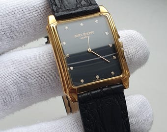 May include: A gold-toned rectangular wristwatch with a black face and diamond hour markers. The watch features the text "PATEK PHILIPPE GENEVE" and has a black leather band.