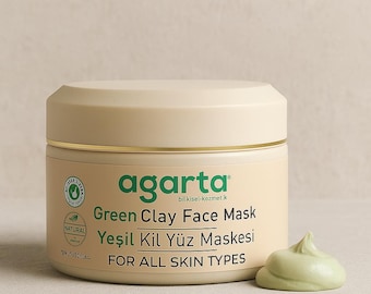 Op de afbeelding: Een pot Agarta Green Clay Face Mask met een monster van lichtgroene crème. De pot is gebroken wit met gouden rand en groene tekst. De tekst op de pot luidt "Green Clay Face Mask" en "FOR ALL SKIN TYPES."