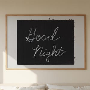 May include: A bedroom scene featuring a bed with a beige checkered comforter and pillows. A framed artwork with the words "Good Night" in white script hangs above the bed. A gold lamp sits on a wooden nightstand.