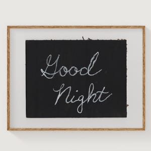 Op de afbeelding: Een ingelijst kunstwerk met de woorden "Good Night" in witte letters op een zwarte achtergrond. Het kunstwerk zit in een lichtbruine houten lijst met een transparante afdekking, geschikt voor slaapkamerdecoratie.