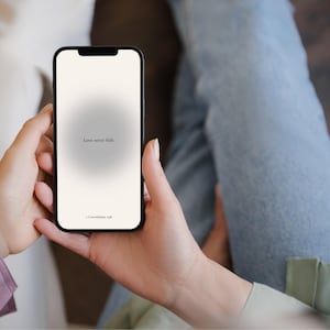 Puede incluir: Un smartphone negro muestra el texto "Love never fails" sobre un fondo degradado. El teléfono está sostenido por dos manos, con el texto "1 Corintios 13:8" en la parte inferior. La pantalla del teléfono es el foco principal.