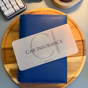 May include: A rectangular, translucent plastic card with rounded corners featuring the text CAR INSURANCE and the smaller text KIMMYPBUDGETS, layered over a vibrant blue, textured, pebble-grain leather binder with a vertical orientation.