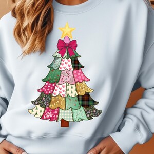 May include: Pale blue sweatshirt with a festive Christmas tree design. The tree is made up of patchwork patterns in green, pink, and gold, with a pink bow and a yellow star at the top. A comfortable, casual style.