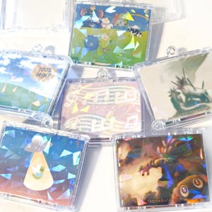 May include: A collection of clear plastic CD cases, each containing a unique holographic image. The images vary, including landscapes, cartoon characters, musical notes, and a UFO. Some cases have text, such as "100% legit" and a website address.