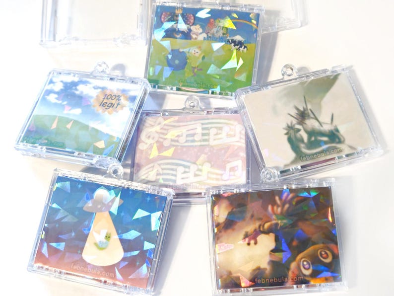 May include: A collection of clear plastic CD cases, each containing a unique holographic image. The images vary, including landscapes, cartoon characters, musical notes, and a UFO. Some cases have text, such as "100% legit" and a website address.
