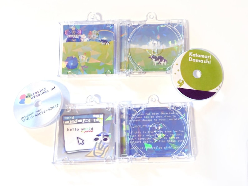 May include: A collection of CDs and CD cases with colorful graphics. One CD case features a cow in a field, another displays a computer error message. Other CDs have text that reads "microstop winblows xd" and "Katamori Damashi".