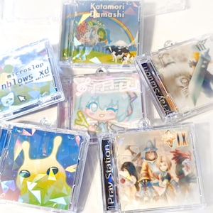 Op de afbeelding: Een verzameling doorzichtige plastic cd-hoesjes, elk met kleurrijke illustraties. De hoesjes tonen diverse ontwerpen, waaronder anime-stijl personages, abstracte patronen en game-gerelateerde graphics. Sommige hoesjes hebben de tekst "Play Station".