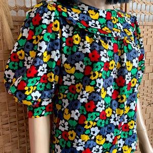 May include: A black blouse with a colourful floral print. The flowers are red, yellow, green and blue. The blouse has a Peter Pan collar and short, puffed sleeves.