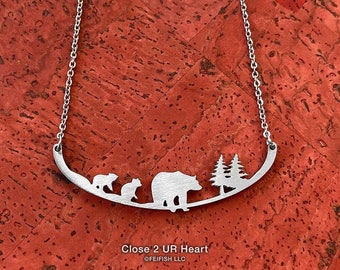 May include: A silver necklace with a bear family and pine trees silhouette charm. The charm is curved and says "Close 2 UR Heart" and "©FEIFISH LLC".