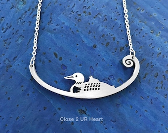 May include: Silver necklace with a loon and chick cutout design. The pendant is shaped like a crescent moon and has the words "Close 2 UR Heart" engraved on the bottom.