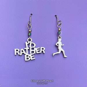 May include: A pair of silver earrings. One earring features the words "I'd Rather Be" in a jumbled design. The other earring features a silhouette of a runner.