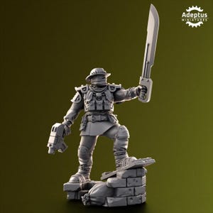 Puede incluir: Figura en miniatura gris de un soldado con sombrero y uniforme, sosteniendo una gran espada y una pistola. La figura está de pie sobre una estructura de ladrillos con un saco. El logotipo de Adeptus Miniatures está en la esquina superior derecha.