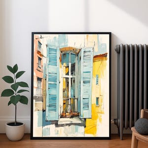 Puede incluir: Impresión artística enmarcada de una fachada de edificio con una ventana abierta y contraventanas azules. La obra de arte presenta un estilo impresionista colorido con tonos amarillos, azules y naranjas. La impresión se muestra sobre un suelo de madera.