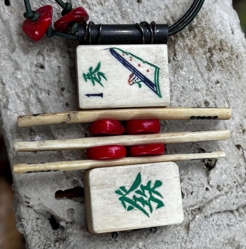 May include: A handcrafted necklace featuring a pendant made from vintage Mahjong tiles. The pendant has a black cord and is accented with red beads. The tiles display green and blue artwork and Chinese characters.