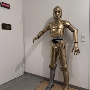 以下が含まれることがあります： メタリック仕上げの等身大の金色の人型ロボットフィギュア。右下の脚部が銀色になっているのが特徴です。ロボットは円形のアイポートを備えた丸みを帯びた頭部、分割された胴体、関節のある腕と脚を持っています。