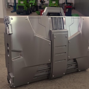 Può includere: Una valigetta in metallo argentato dal design futuristico. La valigetta ha una forma rettangolare con vari pannelli, rivetti e una maniglia. L'estetica generale suggerisce un tema high-tech o industriale.