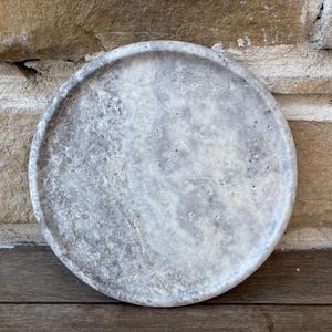 May include: A round, gray and white marble coaster with a smooth, polished surface.