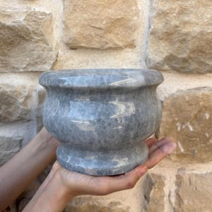 May include: A gray marble planter with a rounded base and a wide, slightly flared opening. The planter is smooth and has a subtle marbled pattern.