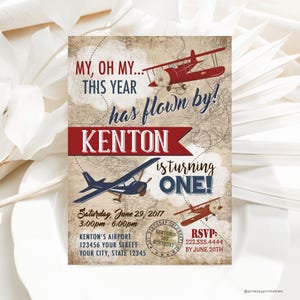May include: A vintage-style airplane themed first birthday party invitation with a red and blue color scheme. The invitation features a red airplane with a white propeller and a blue airplane with a white propeller. The text on the invitation reads "My, oh my... this year has flown by! Kenton is turning one!" and includes the date, time, and location of the party. RSVP information is also included.