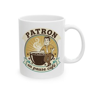 May include: White ceramic coffee mug featuring a cartoon illustration. The design includes a brown coffee cup, a man, and the words "PATRON en pause café" in a vintage style. The mug has a curved handle.