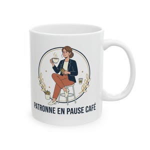 May include: White ceramic mug featuring an illustration of a person sitting and holding a coffee cup and a phone. The illustration is inside a gold circle with the text "PATRONNE EN PAUSE CAFÉ" below. The person is wearing a blazer and pants.