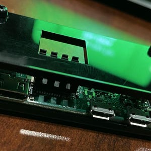May include: A black plastic case with a green light shining through the top. The case has several ports and screws on the side.