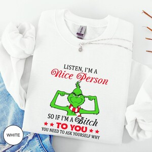 Op de afbeelding: Witte sweatshirt met de tekst "Listen, I'm a Nice Person, so if I'm a Bitch to You, You Need to Ask Yourself Why." De afbeelding toont een groen personage met een rood-witte sjaal. Een zilveren ketting is over de sweatshirt gedrapeerd.