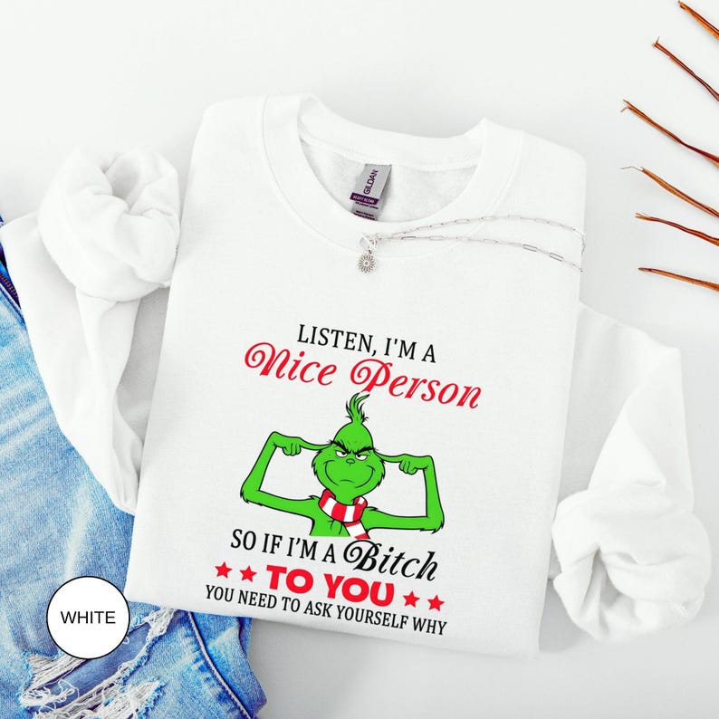 Op de afbeelding: Witte sweatshirt met de tekst "Listen, I'm a Nice Person, so if I'm a Bitch to You, You Need to Ask Yourself Why." De afbeelding toont een groen personage met een rood-witte sjaal. Een zilveren ketting is over de sweatshirt gedrapeerd.