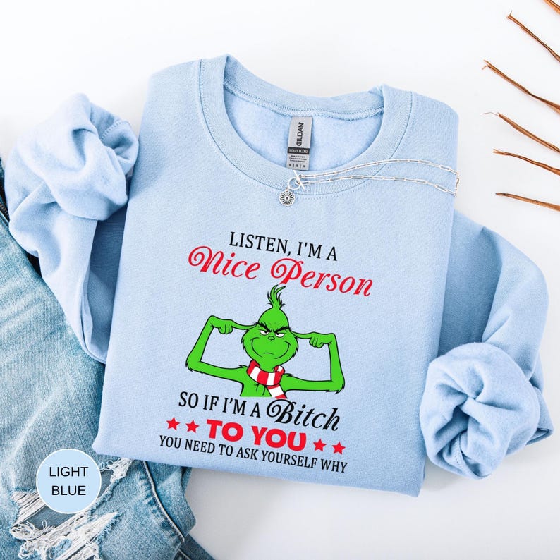 Op de afbeelding: Lichtblauw sweatshirt met de tekst "Listen, I'm a Nice Person, so if I'm a Bitch to you, you need to ask yourself why." Voorzien van een groen stripfiguur met een rood-witte sjaal. Het sweatshirt is van het merk Gildan.
