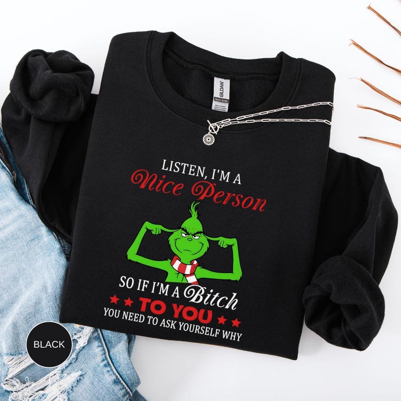 Op de afbeelding: Zwart sweatshirt met de tekst "LISTEN, I'M A Nice Person" in rode letters. Daaronder staat een groen stripfiguur met de tekst "SO IF I'M A Bitch TO YOU YOU NEED TO ASK YOURSELF WHY". Een zilveren ketting ligt over het sweatshirt.