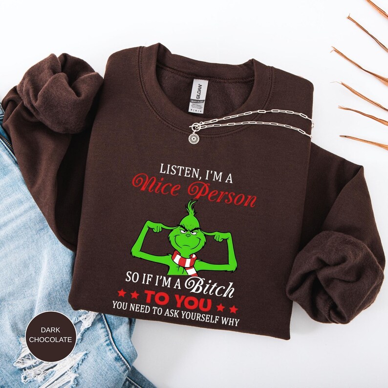 Op de afbeelding: Een donkerbruine sweatshirt met de tekst "LISTEN, I'M A Nice Person" en "SO IF I'M A Bitch TO YOU YOU NEED TO ASK YOURSELF WHY". De afbeelding toont een groen stripfiguur met een rood-witte sjaal.