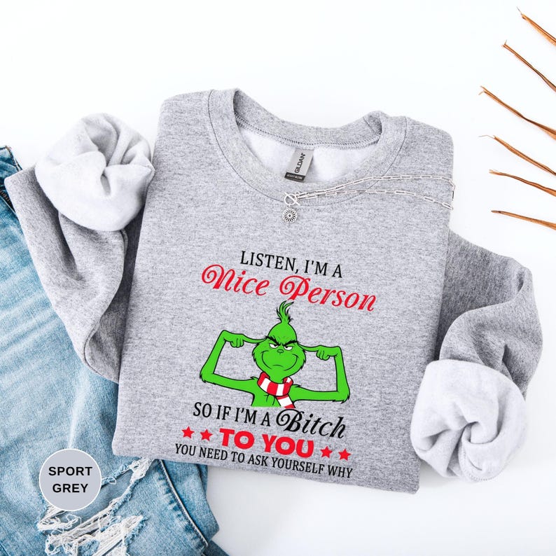 Op de afbeelding: Sportgrijs sweatshirt met de tekst "Listen, I'm a Nice Person" in rode letters boven een groen stripfiguur met een rood-witte sjaal. Daaronder staat de tekst "So if I'm a Bitch to You, You Need to Ask Yourself Why".