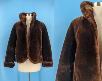 May include: A brown faux fur jacket with a wide collar and long sleeves. The jacket is cropped at the waist and has a relaxed fit.