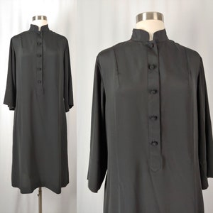 May include: A black dress with a mandarin collar and long sleeves. The dress features a button-down front and a knee-length hemline. The dress is displayed on a mannequin.