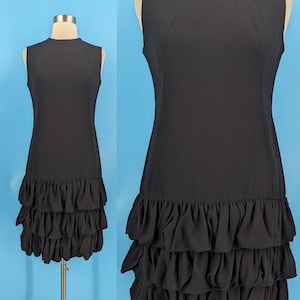 May include: A black sleeveless dress with a fitted bodice and a tiered ruffle skirt. The dress is made of a smooth, lightweight fabric.
