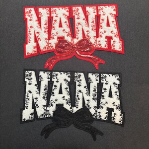 Puede incluir: Dos parches bordados con la palabra "NANA". El parche superior tiene un diseño floral rojo con un lazo rojo. El parche inferior tiene un diseño floral en blanco y negro con un lazo negro. Ambos parches están sobre un fondo gris oscuro.