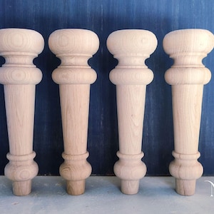 Puede incluir: Cuatro patas de muebles de madera sin terminar con un diseño torneado. Cada pata presenta una parte superior e inferior bulbosas, conectadas por un cuerpo cilíndrico cónico. Las patas son de madera de color claro y están dispuestas sobre un fondo azul oscuro.