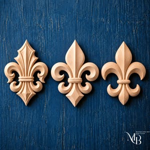 May include: Three light-coloured wooden fleur-de-lis carvings arranged in a horizontal row. Each piece features a central vertical petal flanked by two curved side petals and a horizontal band. The wood has a smooth, natural finish with visible grain.