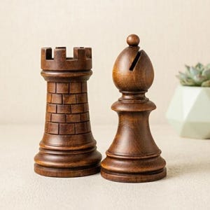 May include: Two dark brown wooden chess pieces standing side by side. On the left is a rook with a crenelated top and brick-like texture. On the right is a bishop with a rounded top featuring a diagonal slit. Both pieces have a smooth base.