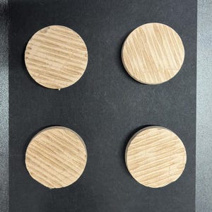 以下が含まれることがあります： 明るい茶色で木目がはっきり見える丸い木片が8つ、黒い面に並んでいます。木片は等間隔に配置されており、1つの木材から切り出されたように見えます。