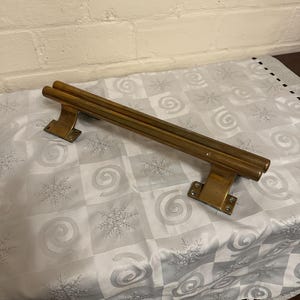 May include: A vintage brass door pull with a rectangular base and a double-bar handle. The hardware is a warm, aged brass colour, showing signs of wear. The door pull is designed for a sturdy and classic aesthetic.