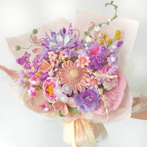 May include: A bouquet of crocheted flowers in shades of lavender, pink, yellow, and green. The arrangement includes various floral shapes, including a large central peach-colored flower, wrapped in light pink tissue paper with a cream ribbon.