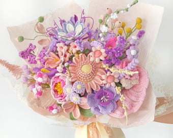 May include: A bouquet of crocheted flowers in shades of lavender, pink, yellow, and green. The arrangement includes various floral shapes, including a large central peach-colored flower, wrapped in light pink tissue paper with a cream ribbon.
