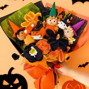 May include: A Halloween-themed bouquet featuring crocheted flowers and characters. The arrangement includes orange pumpkins, witch dolls, and black flowers, all wrapped in orange and black paper. The background is a solid orange with bat and jack-o'-lantern cutouts.