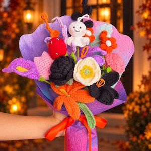 May include: A crochet flower bouquet featuring a white ghost figure, a red strawberry, and various flowers in purple, orange, black, pink, and white. The arrangement is wrapped in purple and blue textured paper and tied with an orange ribbon.
