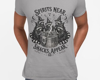 May include: A light gray crew neck t-shirt featuring a black and white graphic of four raccoons wearing wizard hats and robes gathered around a circular table with candles and smoke, with the text SPIRITS NEAR, SNACKS APPEAR printed above and below.